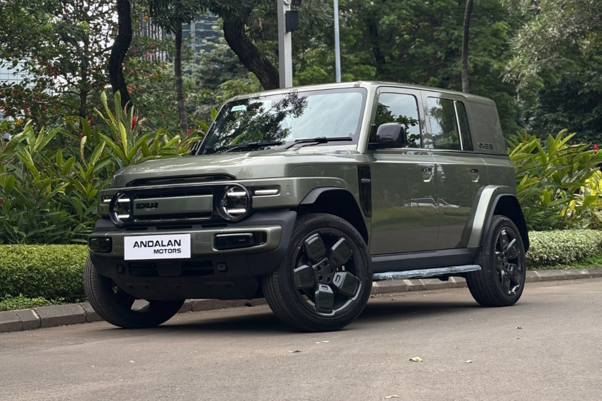 A green off-road vehicle parked on a paved path surrounded by lush greenery and plants.